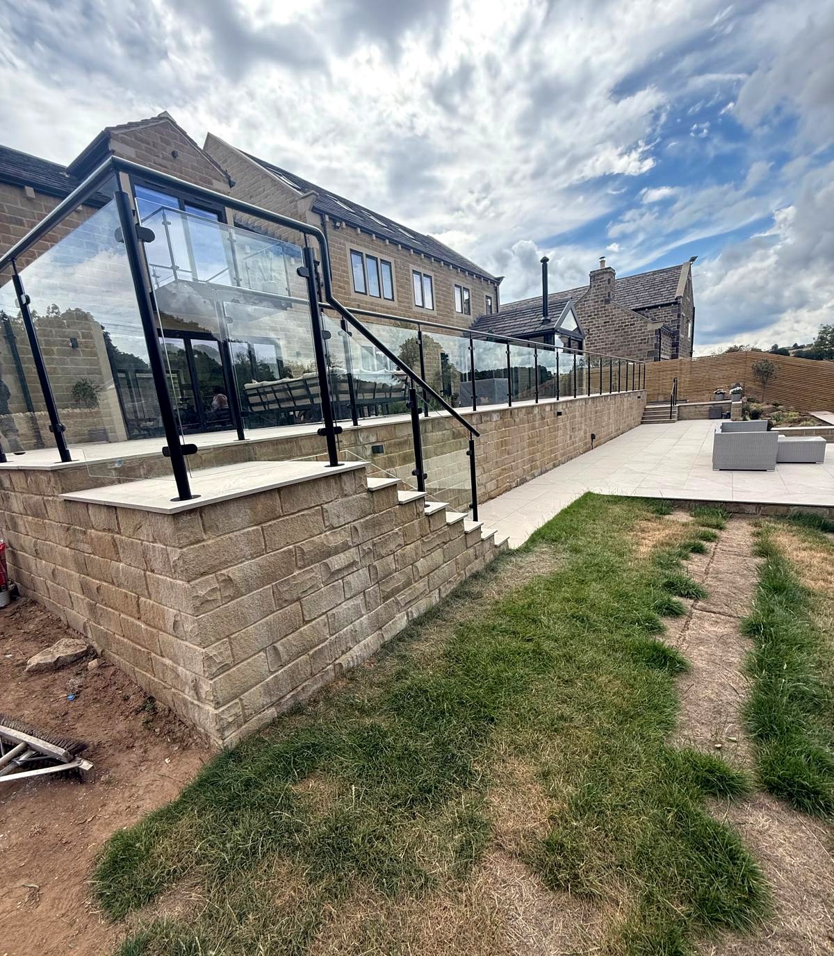 Black galvanised and powder-coated steel and glass balustrade wrapping a raised stone patio at a large home, Sheffield